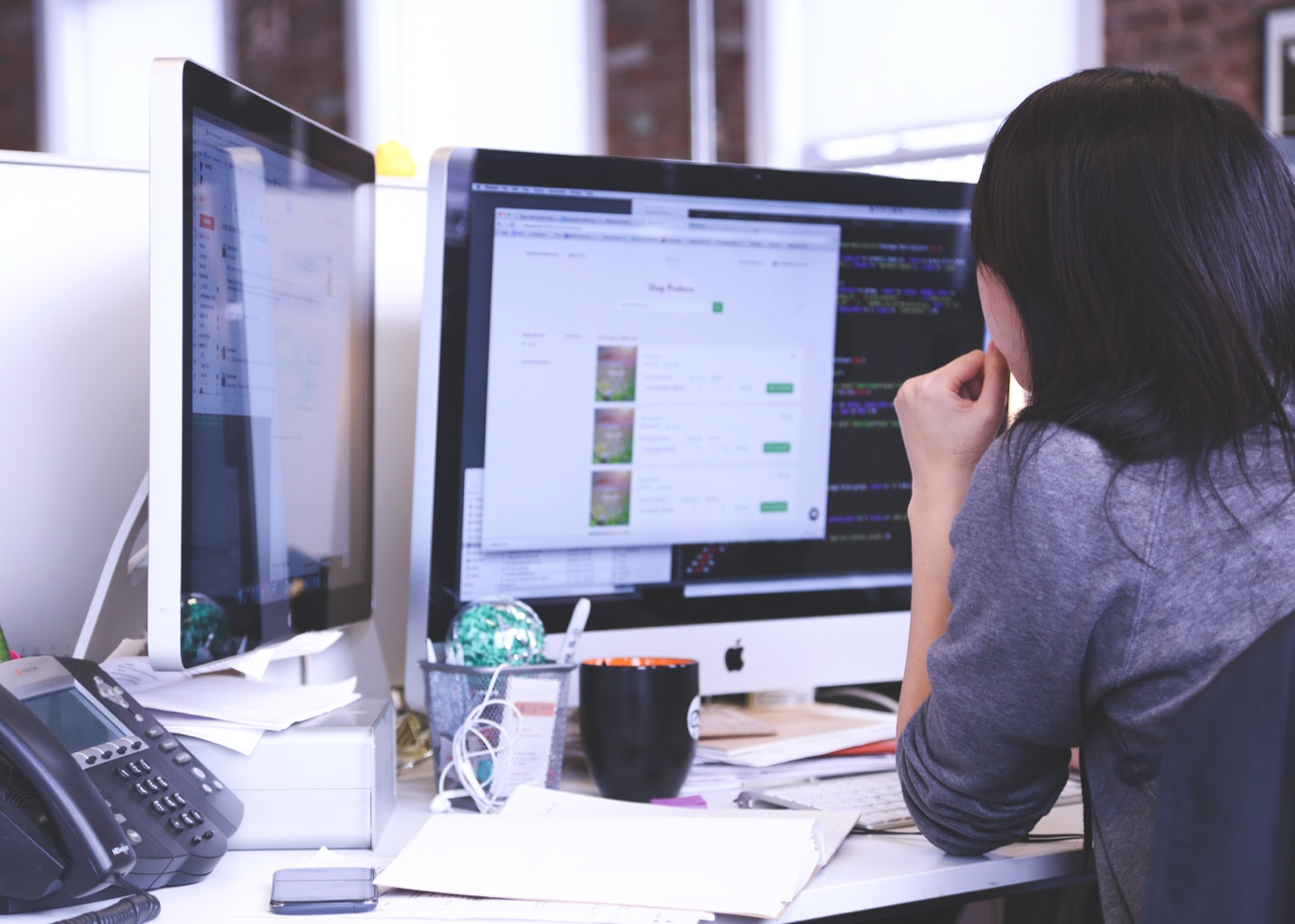 Office worker at a two-monitor desk beside a desk phone and paperwork